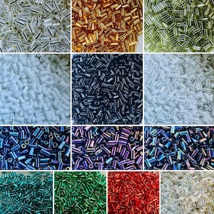 May include: A collection of twelve distinct piles of small, cylindrical glass bugle beads in various colors including silver, gold, olive green, white, black, iridescent blue, purple, teal, emerald green, red, and clear with a metallic finish.