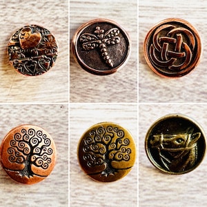 May include: A collection of six decorative metal buttons with various embossed designs. The buttons feature designs such as a heart, dragonfly, Celtic knot, tree of life, and a horse head. The buttons are in shades of copper, bronze, and gold.