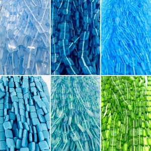May include: Assortment of glass beads in various shades of blue and green. The beads are arranged in rows and are all different shapes and sizes.