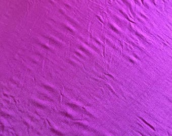 May include: A close-up shot of a vibrant, solid magenta fabric. The material has a soft, slightly wrinkled texture, with subtle variations in tone across its surface. The fabric appears to be lightweight and flowing, suggesting it could be used for clothing or home decor.