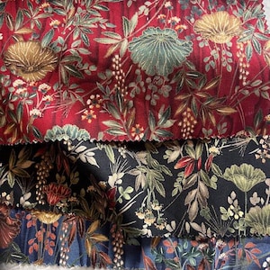 May include: Close-up of three fabric swatches with floral patterns. The top swatch is a deep red with gold and green floral designs. The middle swatch is black with green and red floral designs. The bottom swatch is blue with orange and brown floral designs.