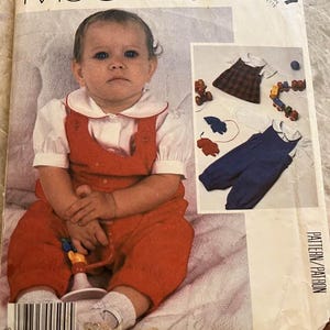 May include: McCall's sewing pattern for baby clothing. The pattern features a baby wearing a red jumpsuit with a white collared shirt. The image includes a close-up of the baby and illustrations of the clothing items. The pattern number is 2217.