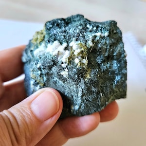 Könnte beinhalten: Ein dunkelgrüner Stein mit eingebetteten weißen und goldenen Kristallen.