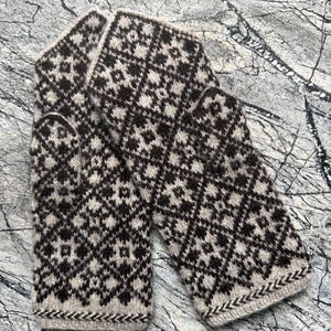 Può includere: Un paio di muffole con un motivo geometrico a rombi marrone scuro e beige. Il tessuto lavorato a maglia presenta un motivo ripetitivo a forma di stella su tutto il corpo, con un bordo a chevron distinto lungo il fondo di ogni muffola.