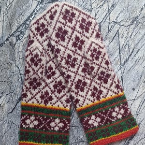 May include: A pair of knitted mittens with a cream-colored background and a repeating burgundy diamond pattern. The cuffs feature bands of green, yellow, and red. These warm mittens are perfect for cold weather.