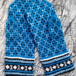 May include: A pair of blue knitted mittens with a geometric pattern in black and white. The mittens have a white and black patterned cuff. The background is a textured, gray surface.