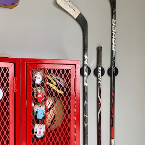 Three CCM and Bauer hockey sticks mounted to the wall near the storage area of a garage using the TwigRig