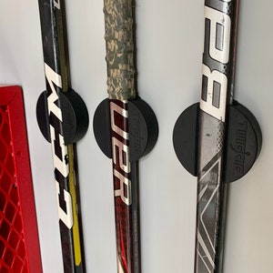 A close up of three CCM and Bauer hockey sticks mounted to the wall near the storage area of a garage using the TwigRig