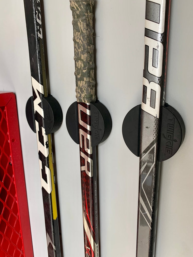 A close up of three CCM and Bauer hockey sticks mounted to the wall near the storage area of a garage using the TwigRig