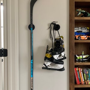 Two TwigRigs mounted to the wall in a bedroom. One of them is holding a Bauer Nexus  hockey stick and the other has a pair of Bauer Supreme skates hanging from it.