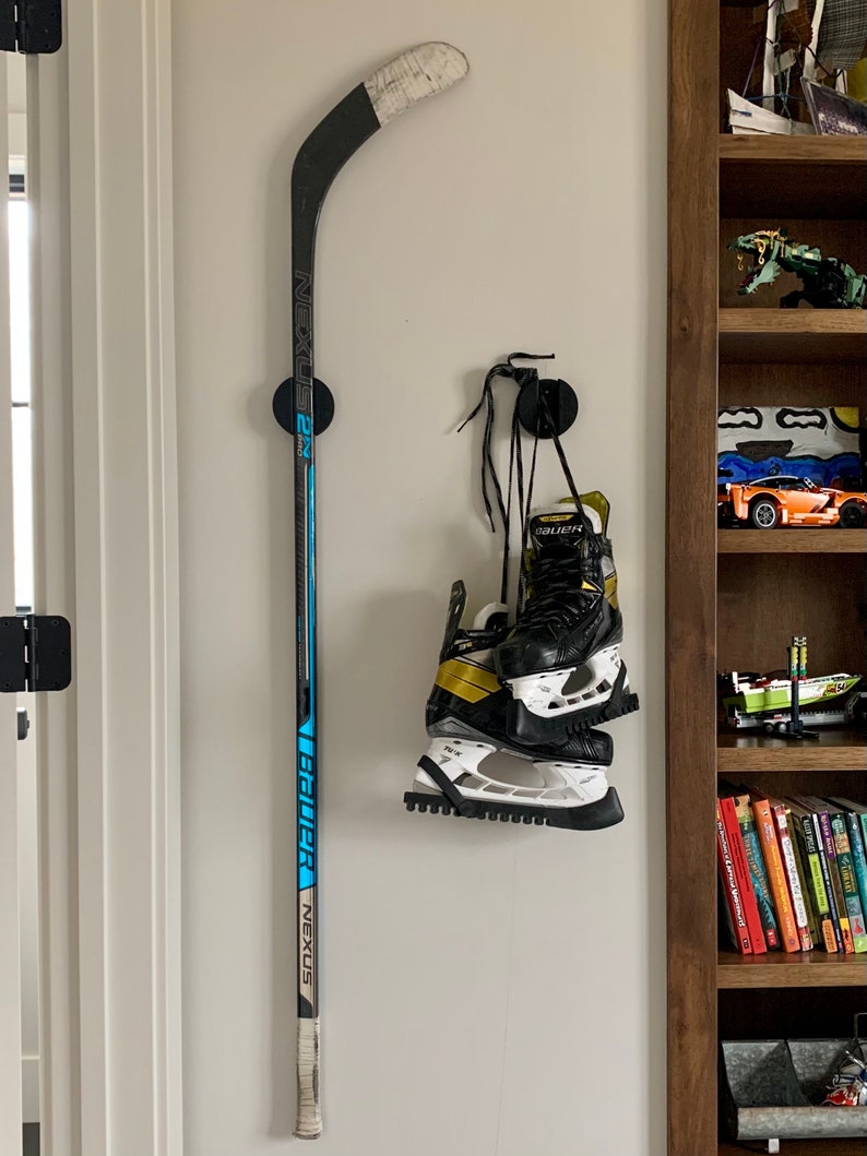 Two TwigRigs mounted to the wall in a bedroom. One of them is holding a Bauer Nexus  hockey stick and the other has a pair of Bauer Supreme skates hanging from it.