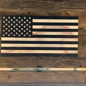 An autographed MN Wild hockey stick mounted to a wall below a USA flag with the TwigRig hockey stick holder