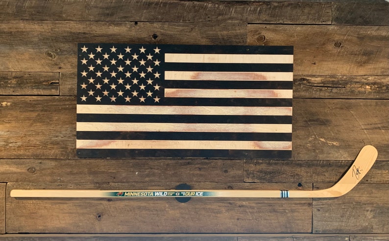 An autographed MN Wild hockey stick mounted to a wall below a USA flag with the TwigRig hockey stick holder