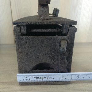 May include: A vintage cast iron charcoal iron with a hinged top and a handle. The iron is approximately 10 inches long and has a ruler for measuring in inches and centimeters.