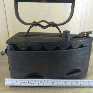 May include: A vintage cast iron charcoal iron with a wooden handle. The iron is approximately 6 inches long and has a series of holes on the bottom.