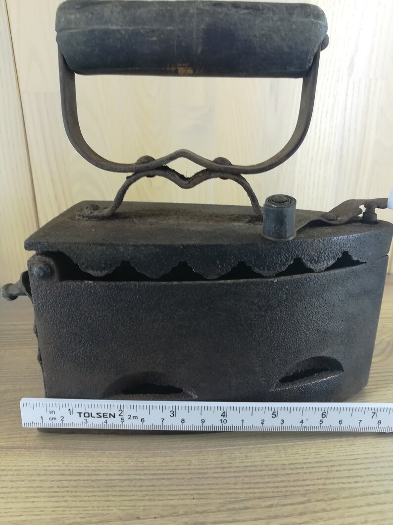 May include: A vintage cast iron charcoal iron with a wooden handle. The iron is approximately 6 inches long and has a series of holes on the bottom.