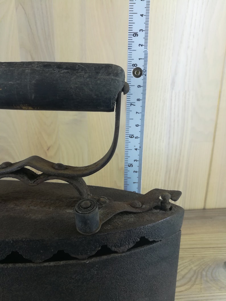 May include: A vintage cast iron flat iron with a wooden handle and a metal latch. The iron is approximately 8 inches tall and has a black finish.