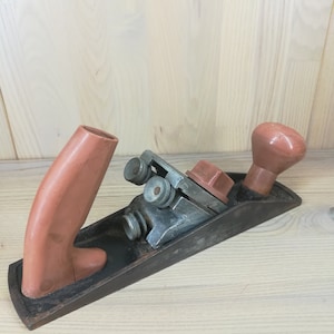 May include: A vintage wooden hand plane with a black metal body and a brown plastic handle. The plane has a metal blade and a metal adjustment knob.