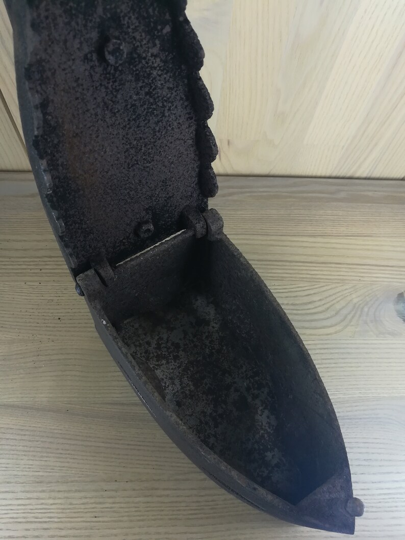 May include: A vintage cast iron flat iron with a hinged lid. The iron is open and the inside is visible. The iron is black and has a rustic appearance.