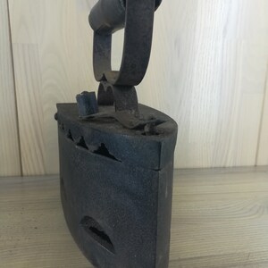 May include: A vintage cast iron flat iron with a wooden handle. The iron has a black finish and is showing signs of wear and tear.