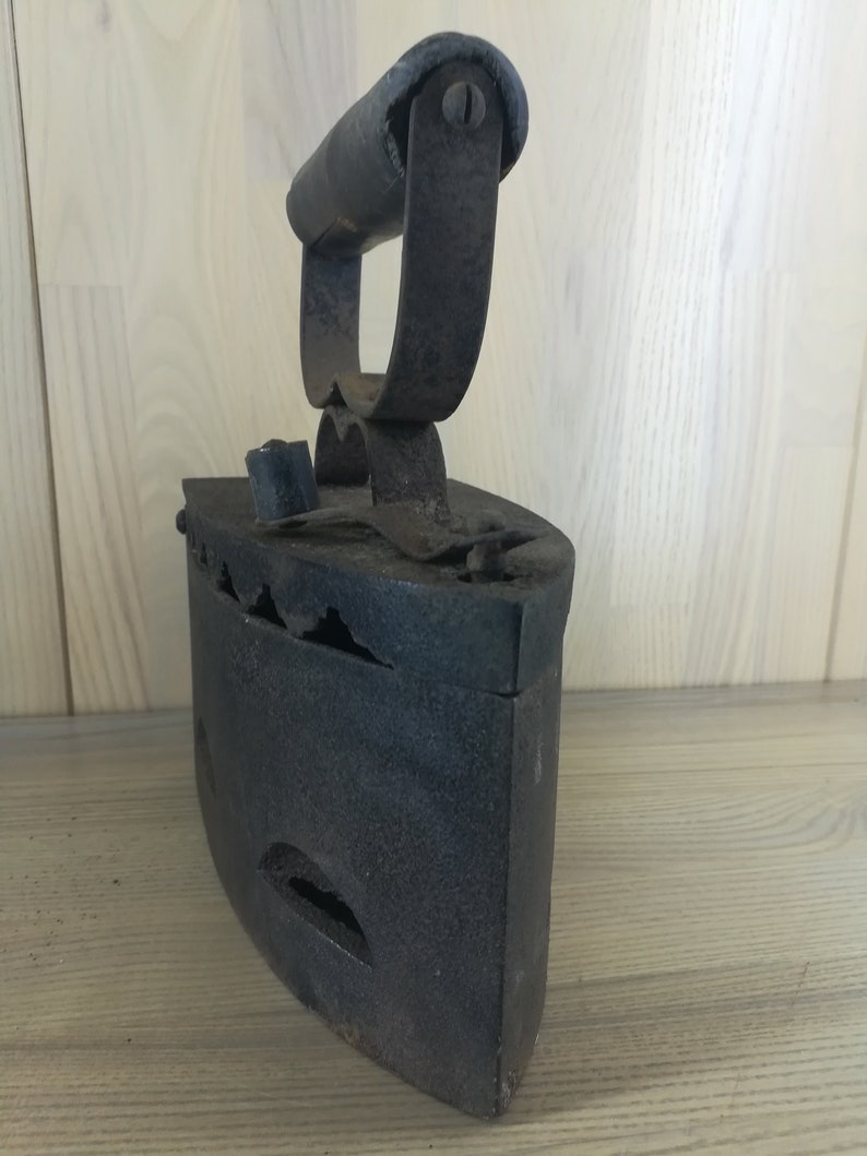 May include: A vintage cast iron flat iron with a wooden handle. The iron has a black finish and is showing signs of wear and tear.