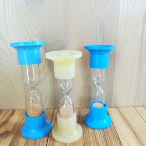 May include: Three blue and white hourglass sand timers with cork stoppers. The sand timers are on a wooden surface.