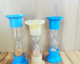 Op de afbeelding: Drie blauwe en witte zandlopers met kurken stoppen. De zandlopers staan op een houten oppervlak.