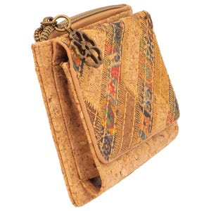 Könnte beinhalten: Eine Korkbrieftasche mit Reißverschluss und dekorativem Anhänger. Die Brieftasche hat ein Patchwork-Design mit farbenfrohen Stickereidetails. Das natürliche Korkmaterial verleiht ihr ein einzigartiges, strukturiertes Aussehen. Sie ist für Karten, Bargeld und andere Essentials konzipiert.