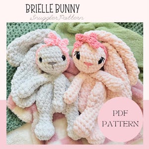 May include: Two crocheted bunny snuggle toys, one gray and one pink, with pink bows on their heads. The toys are sitting on a green and pink blanket. The text "Brielle Bunny Snuggle Pattern" and "PDF PATTERN" is visible in the image.