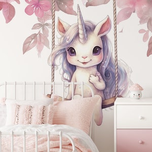 May include: A white unicorn with a pink horn and blue mane sits on a swing in front of a pink floral wall. The unicorn has large, dark eyes and a sweet expression. The swing is made of rope and wood.