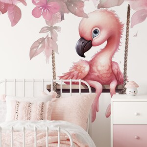 May include: A pink flamingo with blue eyes sits on a swing made of rope and wood. The flamingo is surrounded by pink watercolor leaves and flowers.