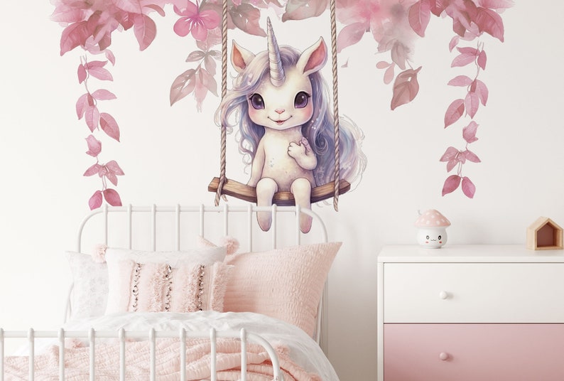 May include: A white unicorn with a pink horn and blue hair sits on a swing made of rope and wood. The unicorn is surrounded by pink flowers and leaves.