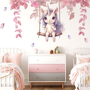 May include: A white unicorn with a pink mane and tail sits on a swing under a pink floral garland. The unicorn is smiling and has a pink horn. There are pink and purple butterflies scattered around the unicorn.