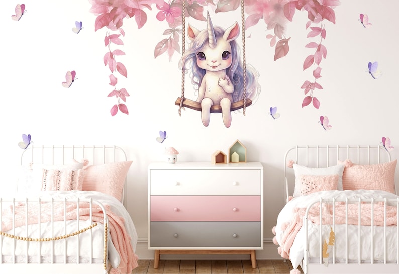 May include: A white unicorn with a pink mane and tail sits on a swing under a pink floral garland. The unicorn is smiling and has a pink horn. There are pink and purple butterflies scattered around the unicorn.