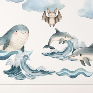 Puede incluir: Un conjunto de pegatinas de pared con una ballena azul, dos delfines, un murci&eacute;lago marr&oacute;n y nubes azul claro. La ballena y los delfines saltan sobre olas azules con espuma blanca, mientras el murci&eacute;lago aparece bajo una nube.