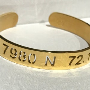 May include: Gold-toned metal bracelet with the coordinates "21.7980 N 72.17" engraved on it.