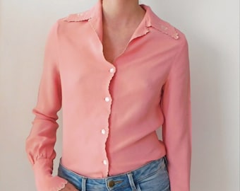 May include: A pink long-sleeve blouse with a scalloped collar and cuffs. The blouse has a button-up front and is made of a lightweight fabric.