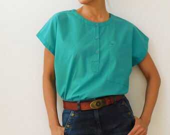 May include: A turquoise short-sleeved shirt with a round neckline and a button placket. The shirt is tucked into a pair of blue jeans with a brown belt.