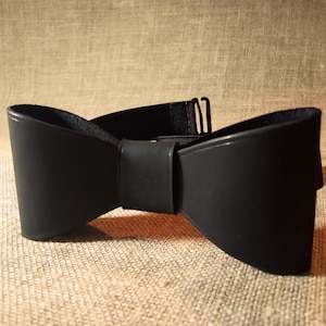 May include: A black leather bow tie with an adjustable strap. The bow tie is made from soft, supple leather and has a classic, elegant design.