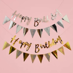 May include: Two gold and silver happy birthday banners with chevron patterned flags. The banners are strung together with clear string.