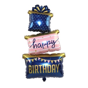 May include: Three blue and gold foil balloons stacked on top of each other. The top balloon is a gift box with white polka dots. The middle balloon is pink with white stripes and the words "happy" in gold. The bottom balloon is blue with gold triangles and the word "birthday" in gold.