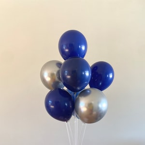 May include: A cluster of blue and silver balloons tied together with clear strings. The balloons are arranged in a pyramid shape.