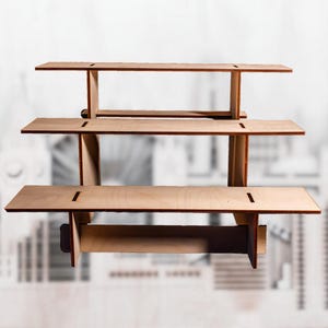 Puede incluir: Un expositor de madera de tres niveles con acabado natural. Cada estante tiene forma rectangular con una ranura en la parte superior. El expositor está diseñado para exhibir productos y tiene una estética sencilla y moderna.