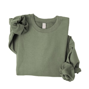 May include: A solid olive green crewneck sweatshirt with long sleeves and a ribbed collar. The garment features a plain, unpatterned fabric texture and a blank white label located at the inside of the neckline, presented against a plain background.