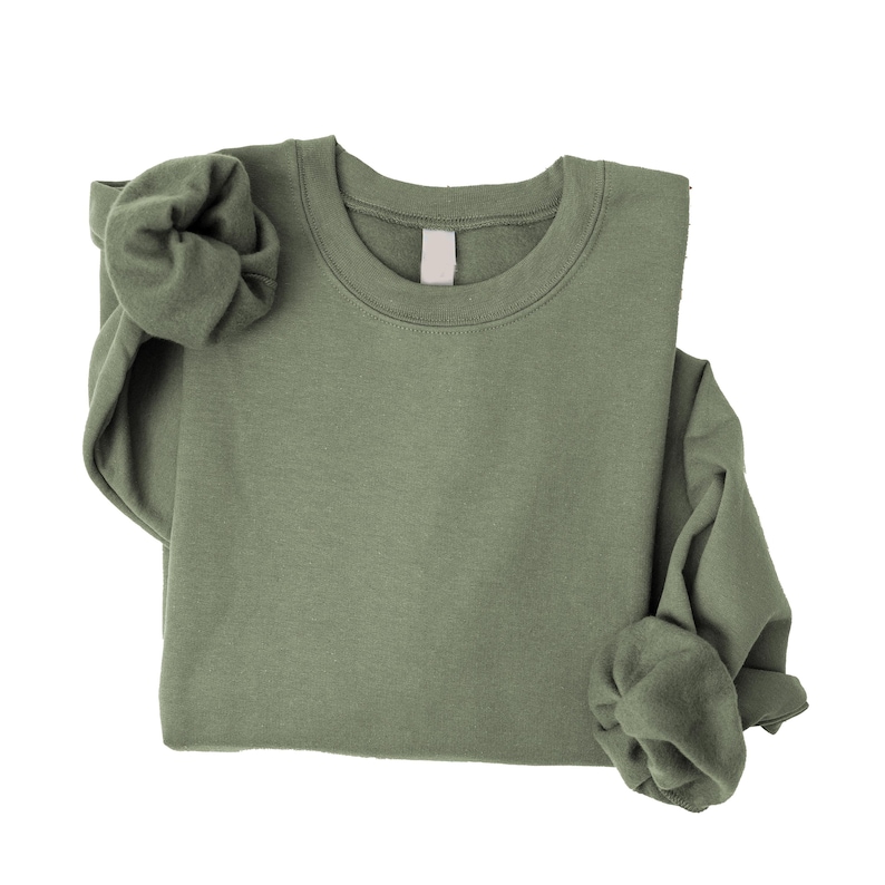 May include: A solid olive green crewneck sweatshirt with long sleeves and a ribbed collar. The garment features a plain, unpatterned fabric texture and a blank white label located at the inside of the neckline, presented against a plain background.