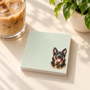 May include: A square, light sage green notepad featuring a detailed illustration of a German Shepherd dog with black and tan fur, pointed ears, and an open mouth with a visible pink tongue, positioned in the bottom right corner.