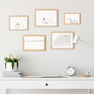 May include: A collection of five framed art prints featuring bird illustrations. The prints are in light wood frames and depict birds perched on branches and wires. The artwork is displayed on a light gray wall above a white desk with a lamp, clock, and flowers.