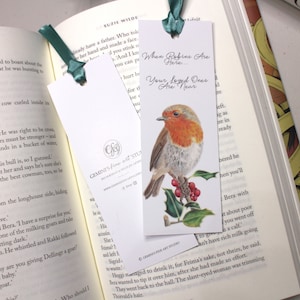 Puede incluir: Dos marcapáginas con una ilustración de petirrojo y el texto "When Robins Are Here... Your Loved Ones Are Near". Los marcapáginas son blancos con una cinta verde atada en la parte superior.