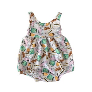 Peut inclure: Une grenouillère blanche pour bébé avec un imprimé rose, vert et marron de camping-cars, de feux de camp et de guimauves.
