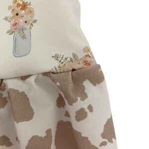 May include: A white fabric with a floral print and a cow print design. The floral print features a bouquet of flowers in a mason jar.